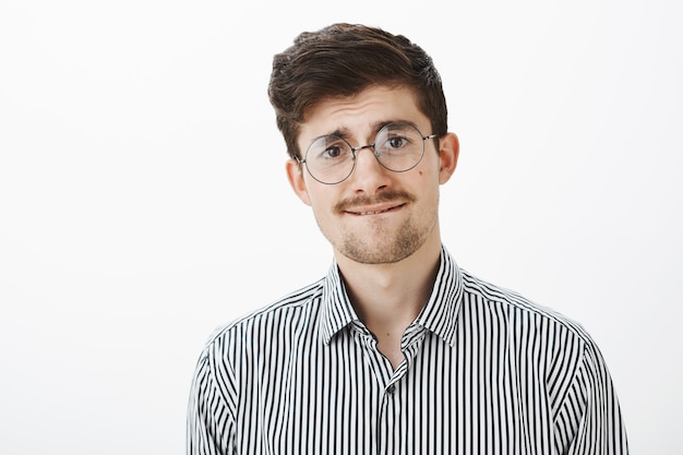 nervous unsure funny bearded guy in round glasses, biting lip and frowning slightly, feeling insecure and unconfident while wanting ask boss about raising payment over gray wall