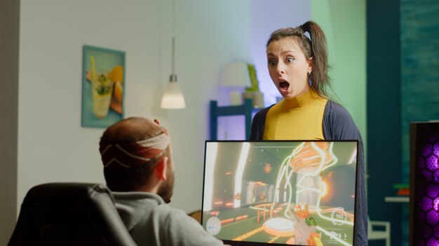 Nervous woman screaming at husband while he is playing space shooter videogame on RGB powerful computer and streaming online competition. Pro cyber with headset performing during virtual tournament