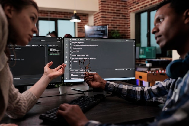 Network developers updating firewall system through information processing using multiple layers of security. Company programmers standing near desk with multiple monitors on top of it.