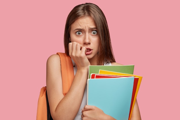 Free photo neurotic puzzled student girl bites finger nails, looks anxiously at camera