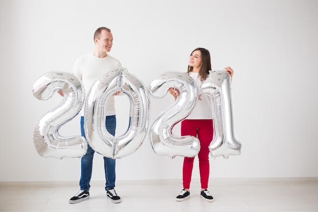 Приближается новый 2021 год - счастливые молодой мужчина и женщина держат в руках серебряные числа