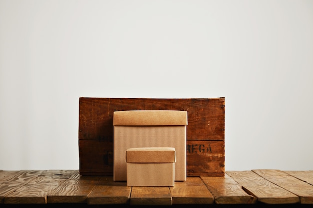 New beige cardboard boxes contrasted against a vintage wine crate and a brown rustic table isolated on white