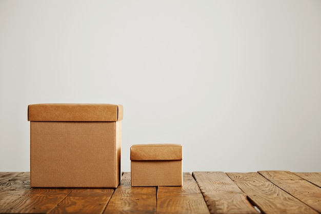 New different sized beige cardboard boxes with covers contrasted against old rough wooden table in a studio with white walls