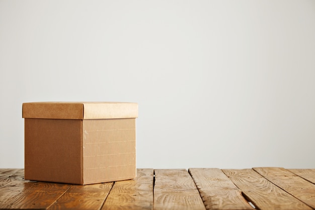 Free photo new fancy square corrugated cardboard box with a cover shot on top of a beautiful rustic table in a studio with white walls