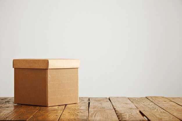 New fancy square corrugated cardboard box with a cover shot on top of a beautiful rustic table in a studio with white walls