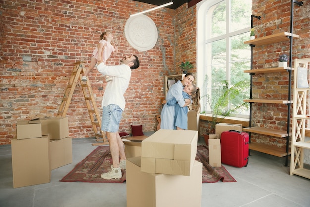 New life. Adult family moved to a new house or apartment. Spouses and children look happy and confident. Moving, relations, new life concept. Unpacking boxes with their things, playing together.