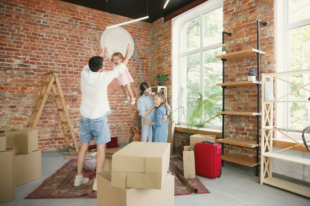 New life. Adult family moved to a new house or apartment. Spouses and children look happy and confident. Moving, relations, new life concept. Unpacking boxes with their things, playing together.