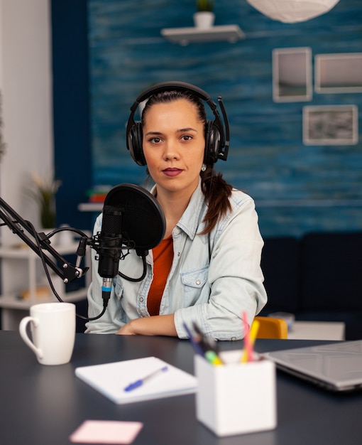New media star looking at camera while talking into microphone during video podcast. Social media influencer recording professional content with modern equipment and digital web internet streaming sta