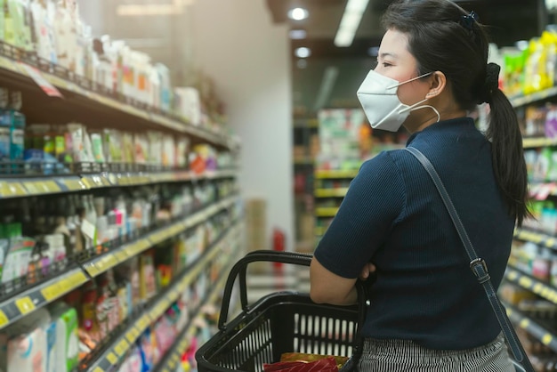 New normal after covid epidemic young smart asian female shopping new lifestyle in supermarket with face shild or mask protection hand choose consumer products new normal lifestyle