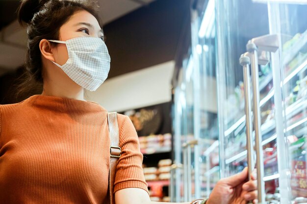 New normal after covid epidemic young smart asian female shopping new lifestyle in supermarket with face shild or mask protection hand choose fresh vegetable of fruit new normal lifestyle