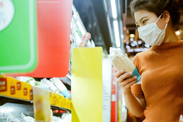 코비드 전염병 후 새로운 정상 젊은 똑똑한 아시아 여성은 슈퍼마켓에서 얼굴 실드 또는 마스크 보호 손으로 새로운 생활 방식을 쇼핑하며 과일의 신선한 야채를 선택합니다.