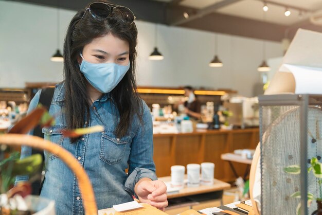 Новый нормальный образ жизни азиатских женщин в синей рубашке носит защитную маску для покупок в универмаге после окончания карантинного периода