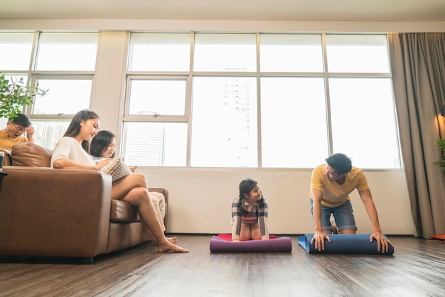 新しい通常のライフスタイルアジアの完全な家族3世代は居間検疫社会的距離活動で喜びホームヨガトレーニングをリラックスします
