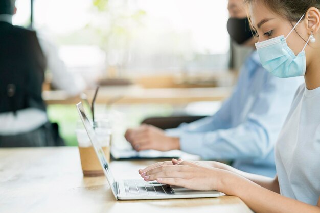 New normal lifestyle concept business people wearing mask sit with social distancing working in public area or co working space with laptop and smartphone