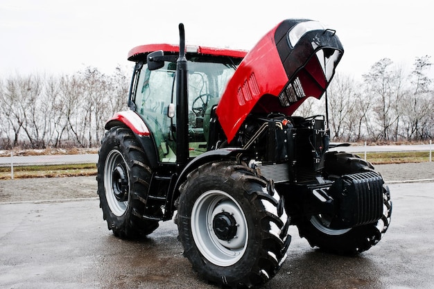 Новый красный трактор с открытым мотором в снежную погоду
