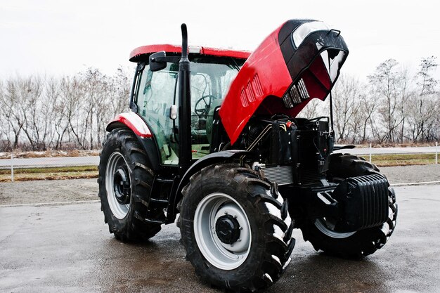 Новый красный трактор с открытым мотором в снежную погоду