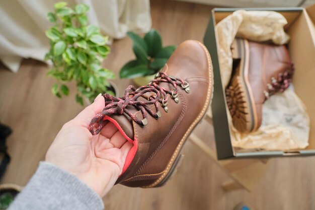 New womens leather brown waterproof hiking winter autumn boots in hands of female, trendy footwear for winter. unpacking shoes, shopping online from home, shoe fashion store