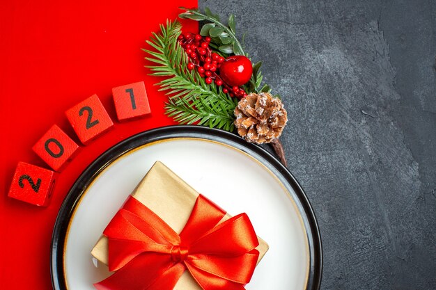 New year background with beautiful gift on a dinner plate decoration accessories fir branches and numbers on a red napkin on a black table half shot photo