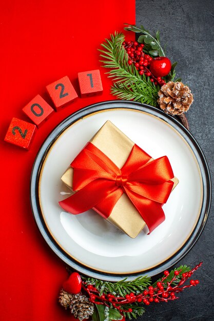 New year background with beautiful gift on a dinner plate decoration accessories fir branches and numbers on a red napkin on a black table vertical view