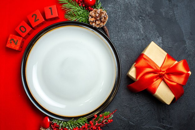 New year background with dinner plate decoration accessories fir branches and numbers and gift on a red napkin on a black table