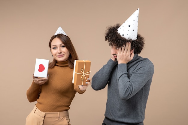 Il concetto di nuovo anno con la bella giovane coppia indossa la ragazza felice del cappello del nuovo anno con il cuore e il regalo