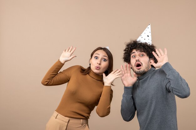 New year concept with shocked young couple wear new year hat looking at something girl and guy on gray