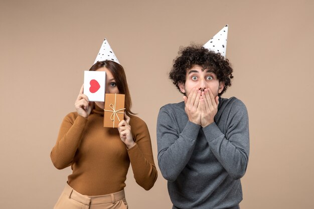 New year concept with young couple wear new year hat girl closing her face heart and gift and shocked guy