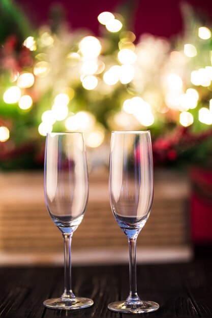 Новогодний праздник или рождественский зеленый фон. Ветки елок украшены золотыми огнями, гирляндами, игрушками и пустыми бокалами из-под шампанского. Ночное освещение. Новогоднее поздравление