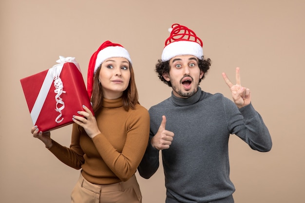 Праздничная концепция новогоднего настроения с забавной возбужденной молодой прекрасной парой в красных шапках санта-клауса на сером