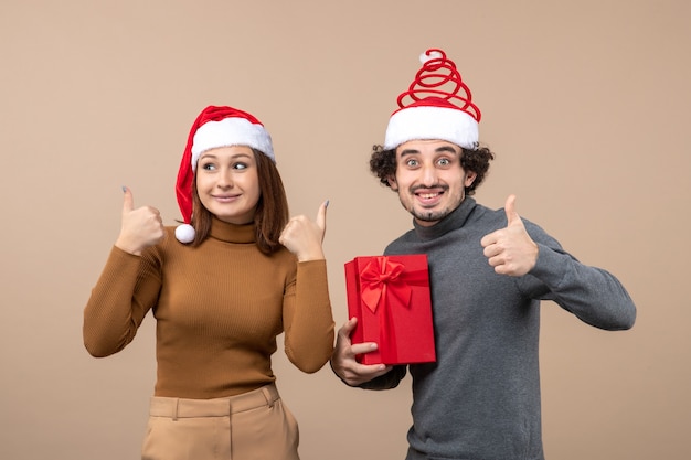 New year mood festive concept with funny happy lovely couple wearing red santa claus hatsmaking perfect gesture on gray