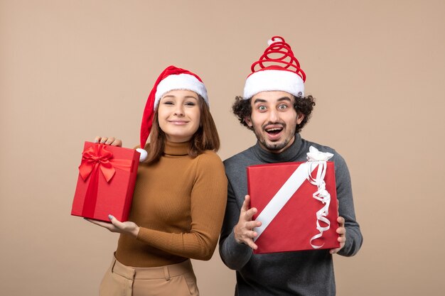 New year mood and party concept - young happy excited lovely couple holding gifts wearing santa claus hats on gray