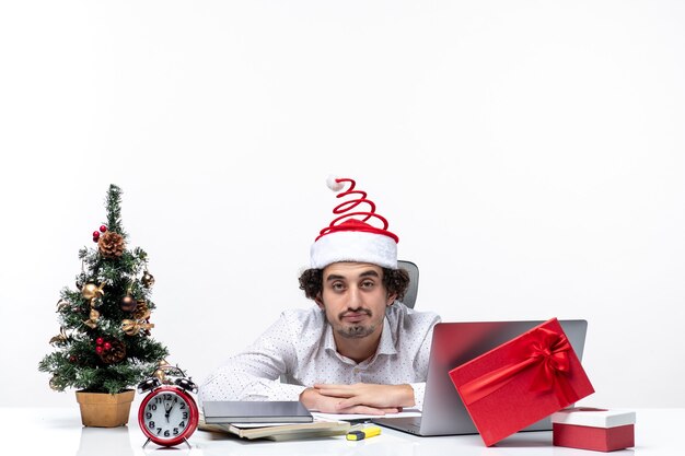 Новогоднее настроение с занятым молодым бизнесменом в забавной шляпе санта-клауса, чувствуя себя усталым от всего в офисе на белом фоне
