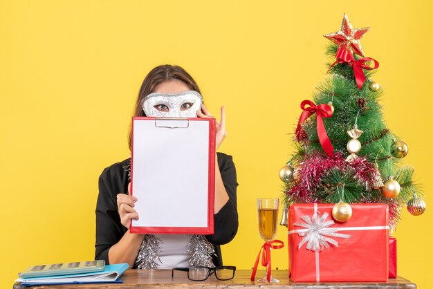 New year mood with charming lady in suit wearing mask and showing document in the office 