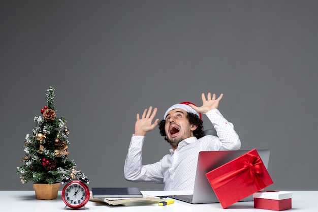 New year mood with shocked excited young businessman with santa claus hat sitting in the office on dark background