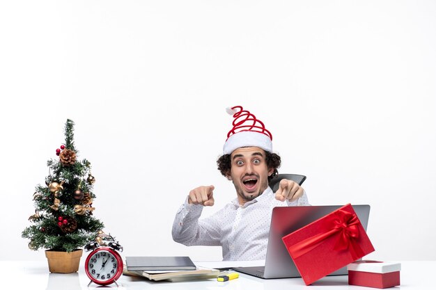 New year mood with smiling excited young businessman sitting in the office and pointing something on white background