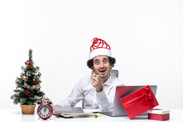 New year mood with surprised smiling excited young businessman with santa claus hat asking about something in the office on white background