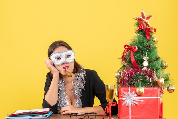 New year mood with thoughtful charming lady in suit wearing mask in deep thoughts in the office on yellow isolated 