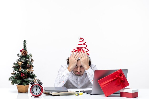 New year mood with young businessman with funny santa claus hat feeling exhausted of everything in the office on white background