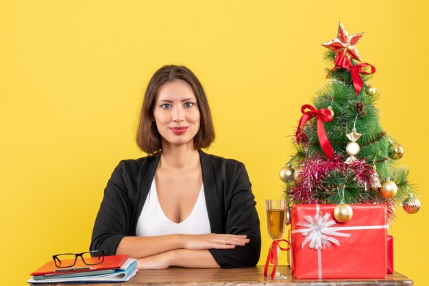 New year mood with young happy emotional business lady sitting at a table in the office on yellow 