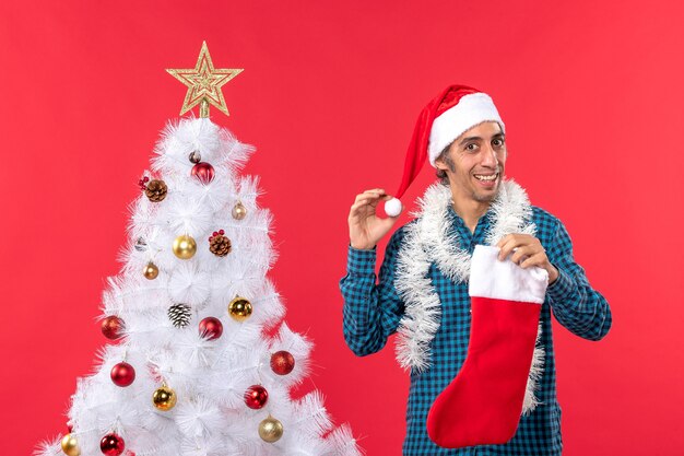 クリスマスの靴下と装飾を保持しているサンタクロースの帽子を持つ若い男と新年の気分