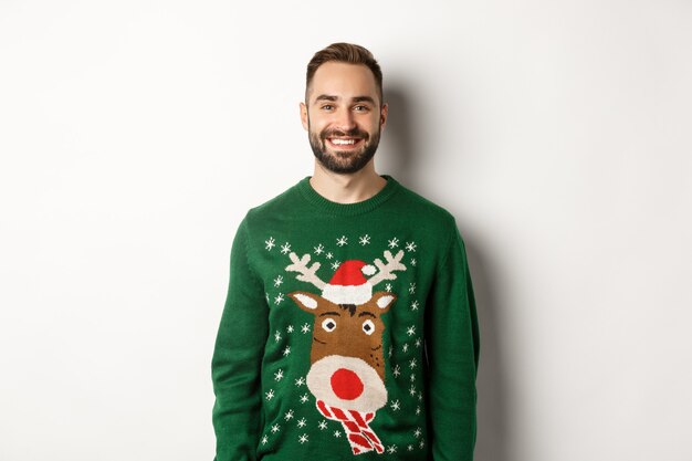 신년 파티와 겨울 휴가 개념입니다. 흰색 배경에 서 있는 재미있는 크리스마스 스웨터를 입은 행복한 수염 난 남자