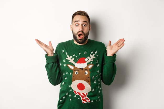 New Year party and winter holidays concept. Surprised bearded guy gasping amazed, standing in Christmas sweater, white background