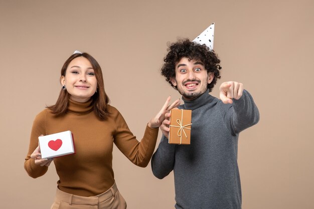 面白い若いカップルと一緒に新年の撮影は、灰色のギフトと心と男と新年の帽子の女の子を着用します