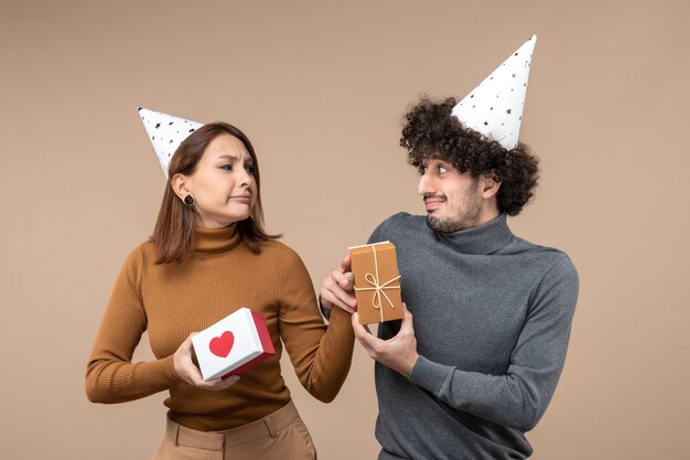 Новогодняя съемка с молодой парой, смотрящей друг на друга, в новогодней шапке с кислым лицом девушка с сердцем