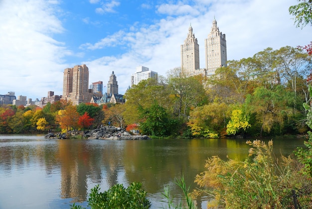 Центральный парк Нью-Йорка осенью с небоскребами Манхэттена и красочными деревьями над озером с отражением.