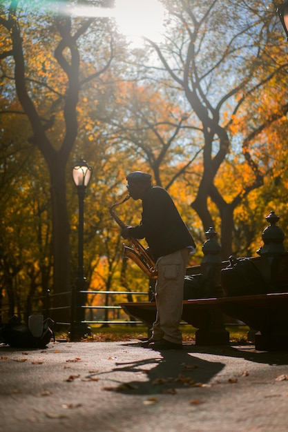 Foto gratuita new york city manhattan central park in autunno. un musicista di strada suona il sassofono a central park a new york city.