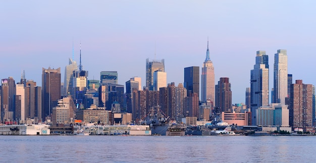 Панорама заката Нью-Йорка на Манхэттене с историческими небоскребами над рекой Гудзон, просматриваемая с набережной Нью-Джерси Уихокен в сумерках со спокойным голубым тоном.