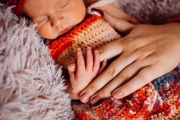 Newborn baby enveloped in red scarf holds mother's finger 