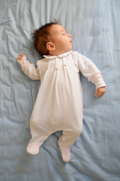 Newborn baby girl sleeping on blue sheets at home