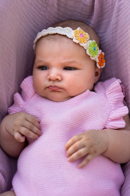 ピンクのニットの服と花の頭のアクセサリーを身に着けている生まれたばかりの女の赤ちゃん